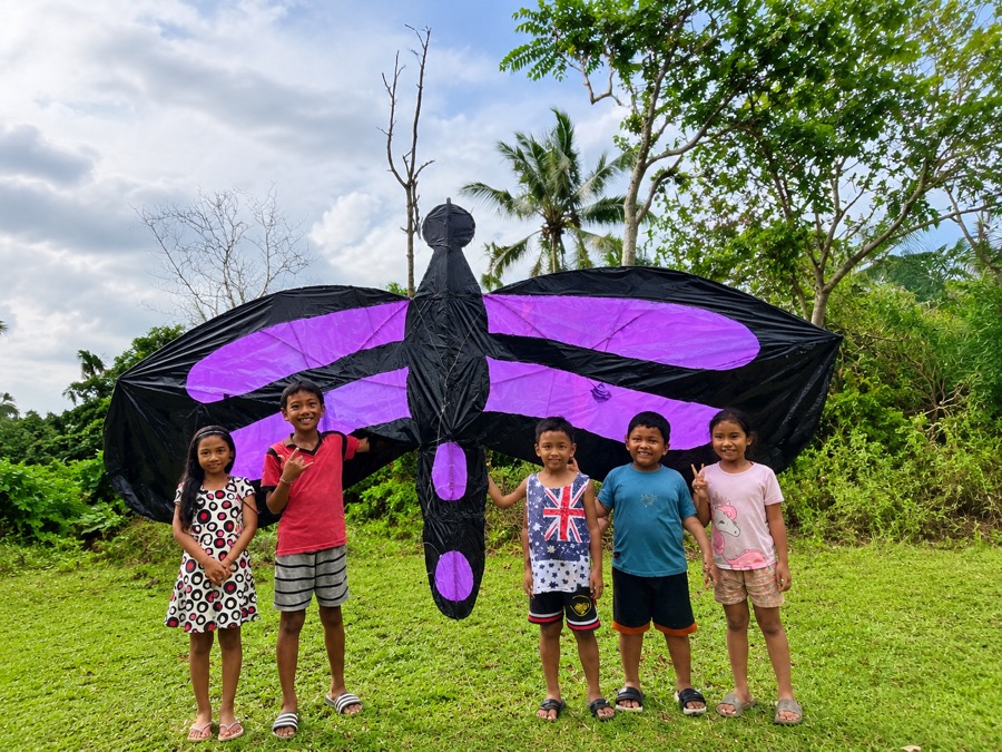 Local children standing with a large handmade kite in rural Karangasem