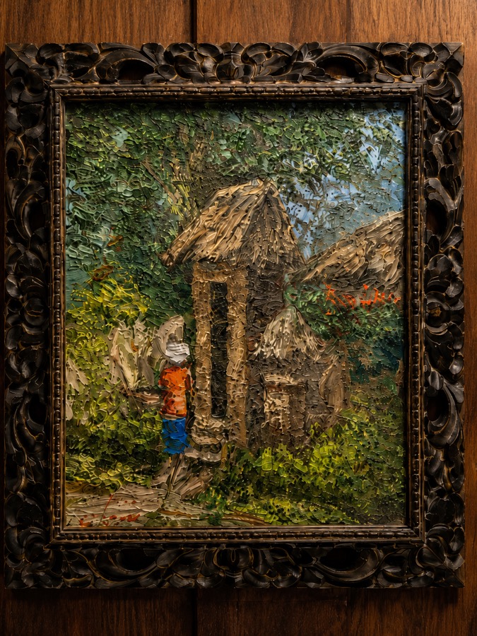 Framed painting by a local artist hanging on wooden walls inside Villa Hola Agung